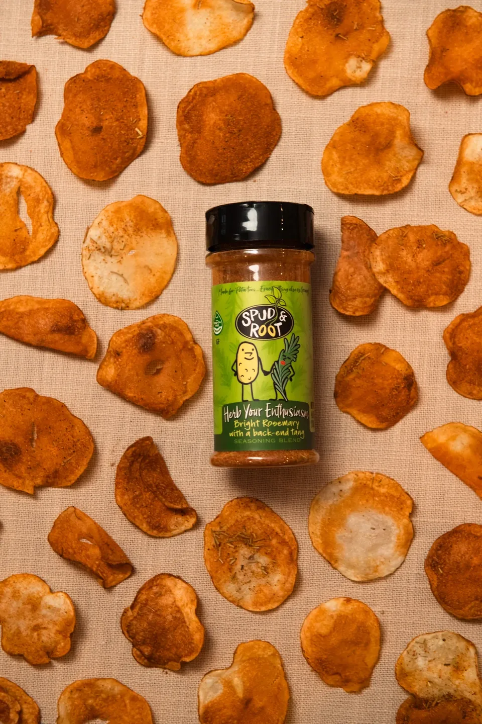 Herb Your Enthusiasm shaker jar lying among round, crisp, orange-brown chips on a pale linen cloth.