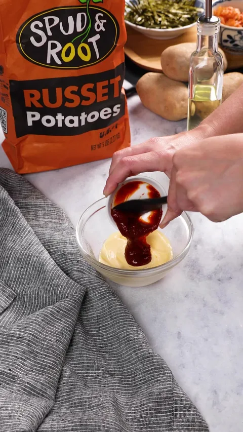 A small cup tipping dark red gochujang into a glass bowl of mayonnaise.