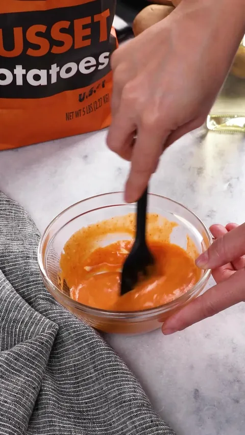 A spatula stirring the spicy mayo, now orange, in the glass bowl.