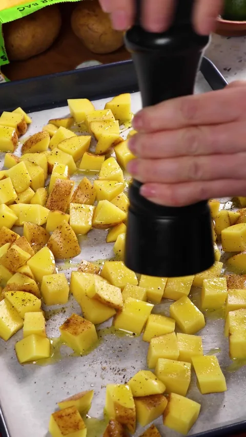 A pepper mill grinding black pepper over the oiled, salted potato cubes.