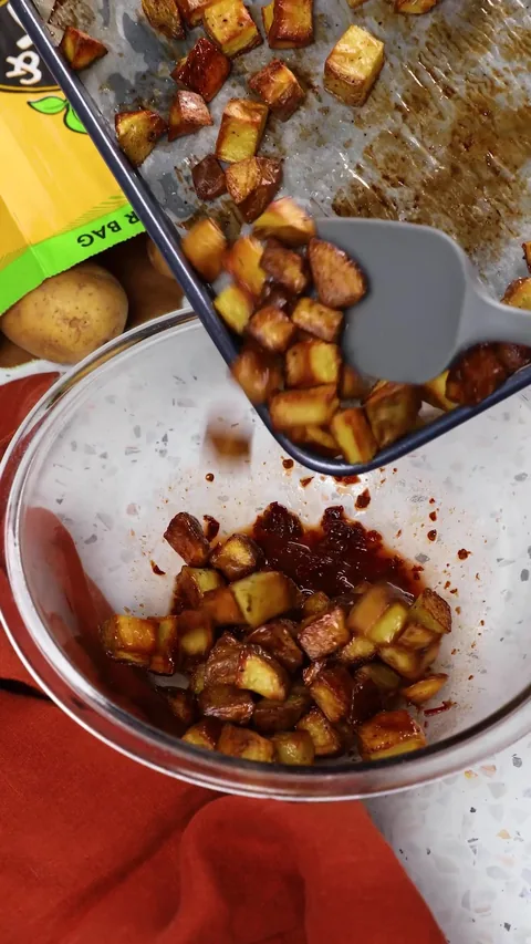 A spatula sliding the roasted potatoes off the baking sheet into the bowl of chipotle sauce.