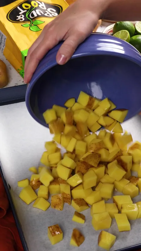 Cubes of Gold potato tumbling from a blue bowl onto a parchment-lined baking sheet.
