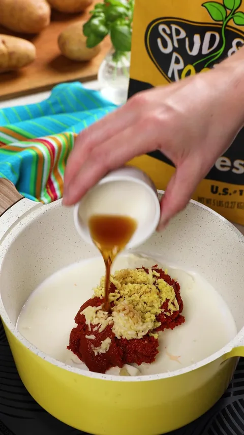 Fish sauce pouring from a small white cup onto the curry paste, ginger and garlic in the pot.