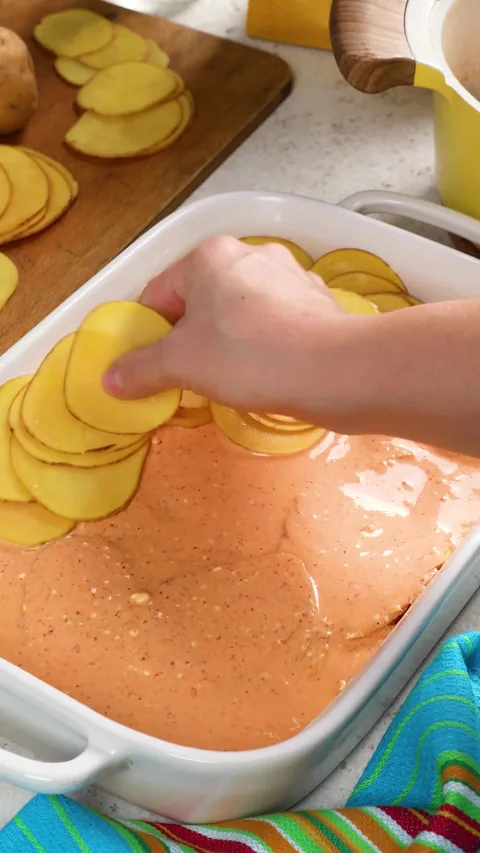A hand adding the last slices of potato over the second layer of sauce.