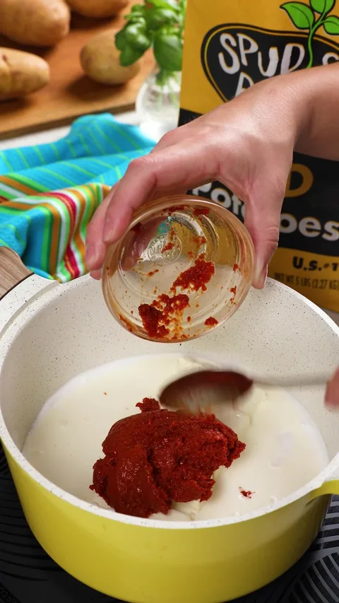 A spoon scraping red curry paste from a small glass bowl into the pot.