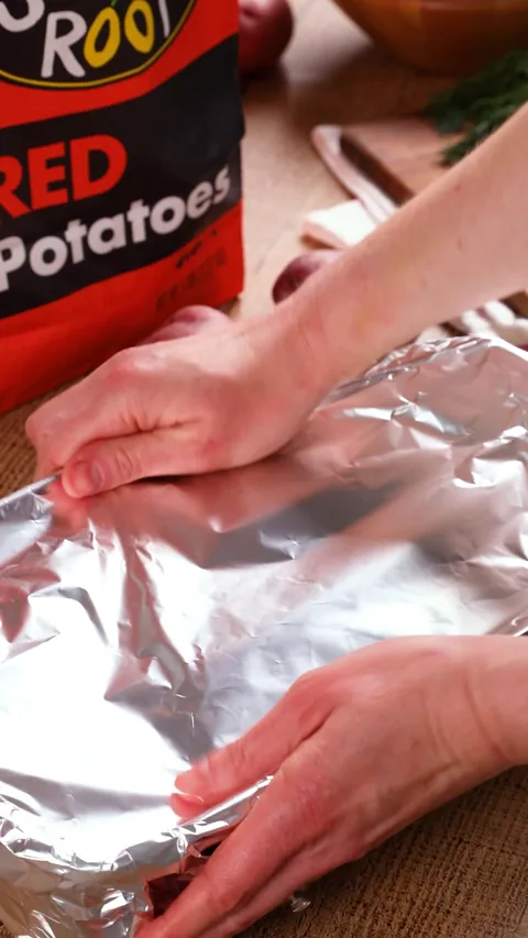 Two hands folding foil over the baking dish.