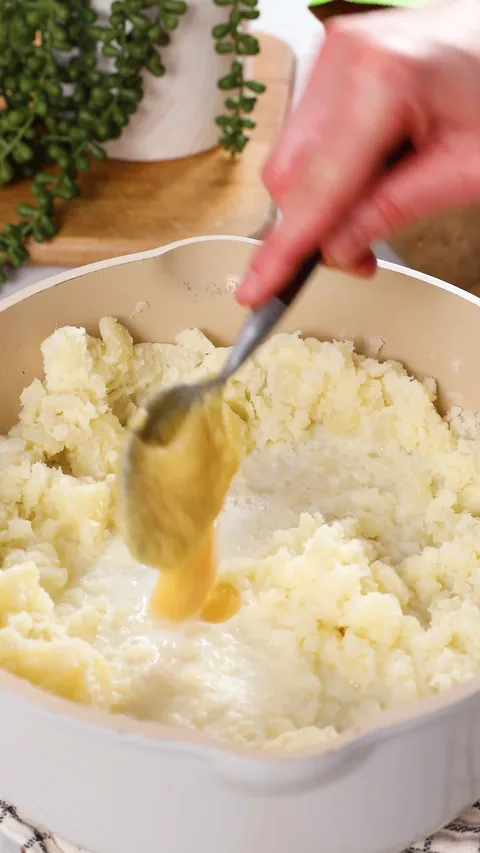 A spoon dripping miso butter onto mashed potatoes in a saucepan.