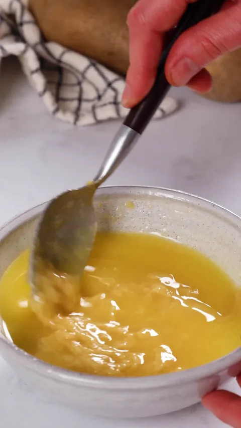 A spoon stirring miso and butter together in a small speckled bowl.