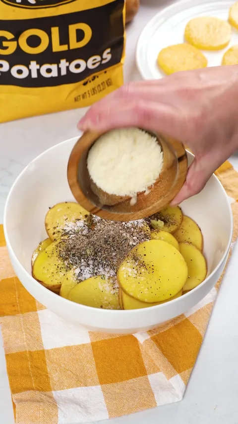 Grated Parmesan tipped from a small wooden bowl over the seasoned potato slices.