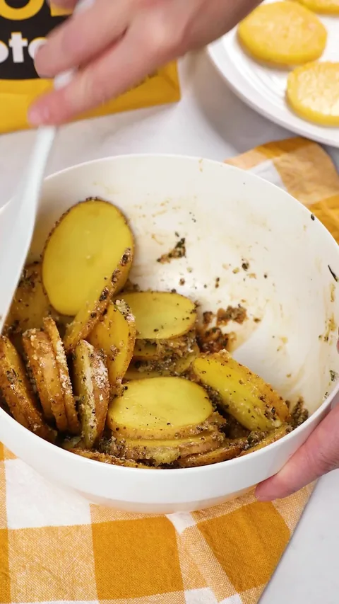 A spoon in the bowl of potato slices, all coated in the herby seasoning.