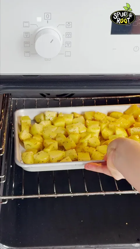 A hand sliding the tray of seasoned potato cubes into the oven.