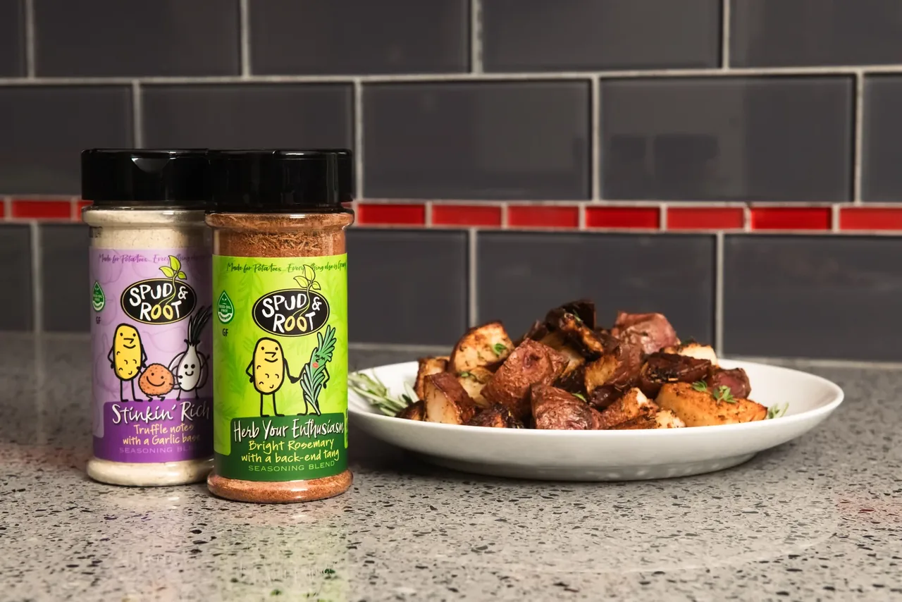 Stinkin' Rich and Herb Your Enthusiasm jars on a kitchen counter beside a plate of roasted potatoes.